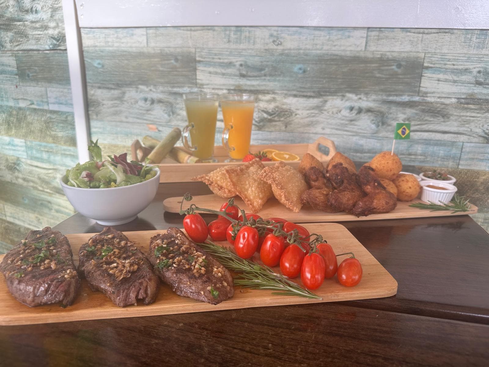 A table at Brasil Burgers: picanha steaks on a board, pastéis, coxinhas, wings and fresh juices